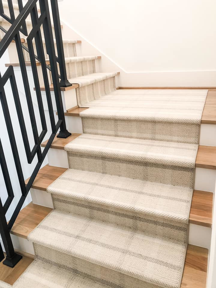 A close-up view of a professionally installed striped carpet runner on a wooden staircase by Southern Star Finishes in Houston, TX.