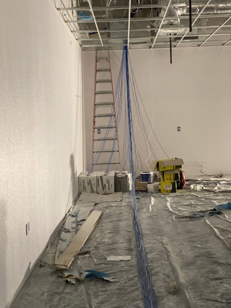 A room under construction with blue structured data cables hanging from the ceiling, showing an installation in progress by CAAM Integration LLC in Albuquerque, NM.