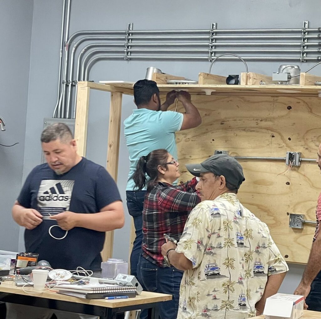 Students practicing electrical conduit bending and wiring on a training board at Escuela Tecnica ABC in North Chicago, IL