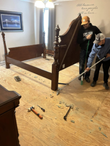 Two contractors sweeping debris from a plywood subfloor after carpet removal by Image Group Flooring in Leesville, SC.