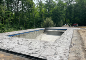 An in-ground swimming pool under construction with a stamped concrete patio by MountainScapes in Nashua, NH.