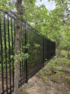 A tall black metal fence installed in a natural wooded area by Stonehenge Fence & Deck in Orem, UT.