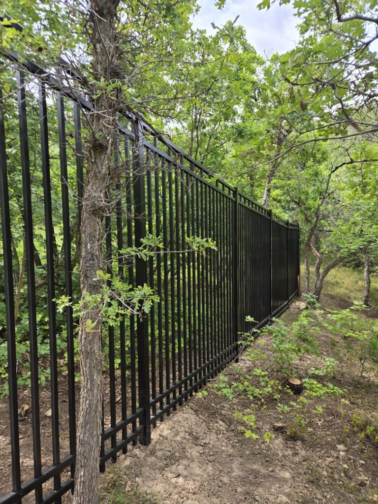 A tall black metal fence installed in a natural wooded area by Stonehenge Fence & Deck in Orem, UT.