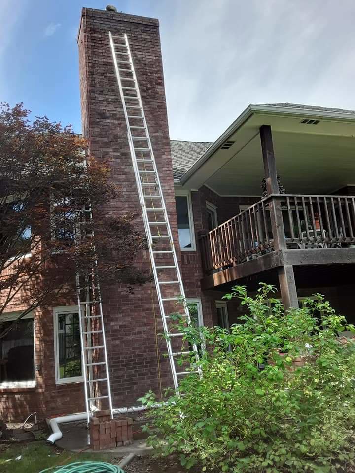 Multiple ladders extending up a very tall brick chimney on a house, indicating a chimney service job by A Step Above Chimney & Siding in Wichita, KS.