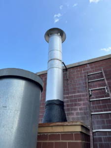 A tall metal chimney flue on a brick building, ready for inspection by Chimney Sweep Service LLC in Brooklyn, NY.