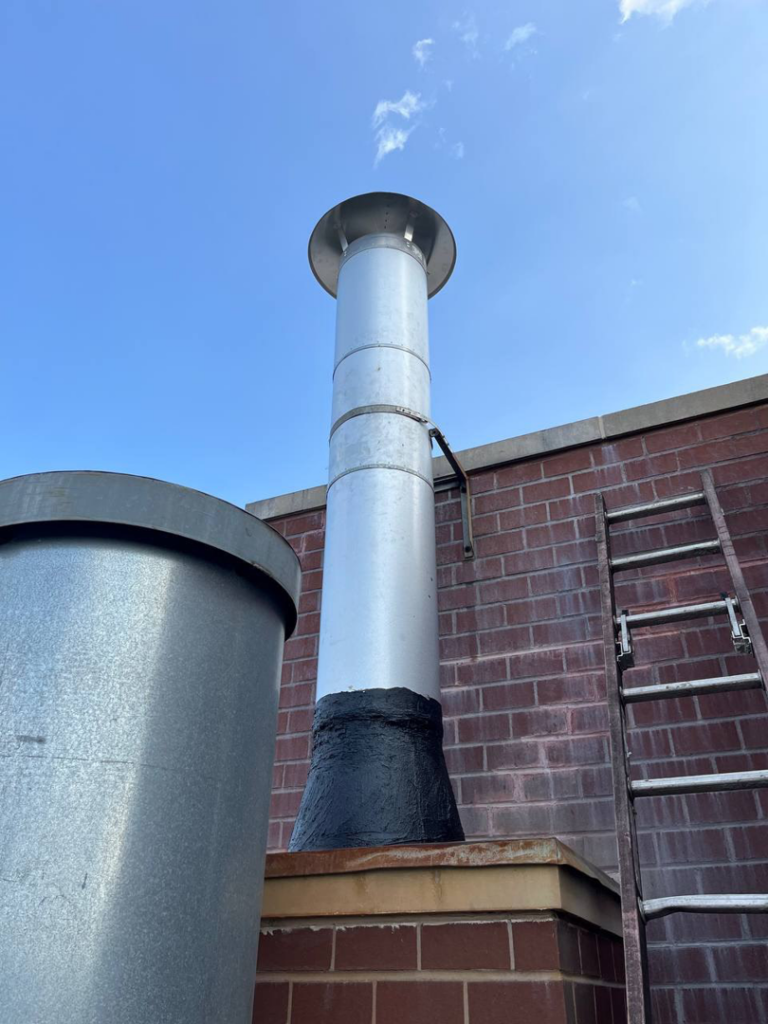 A tall metal chimney flue on a brick building, ready for inspection by Chimney Sweep Service LLC in Brooklyn, NY.