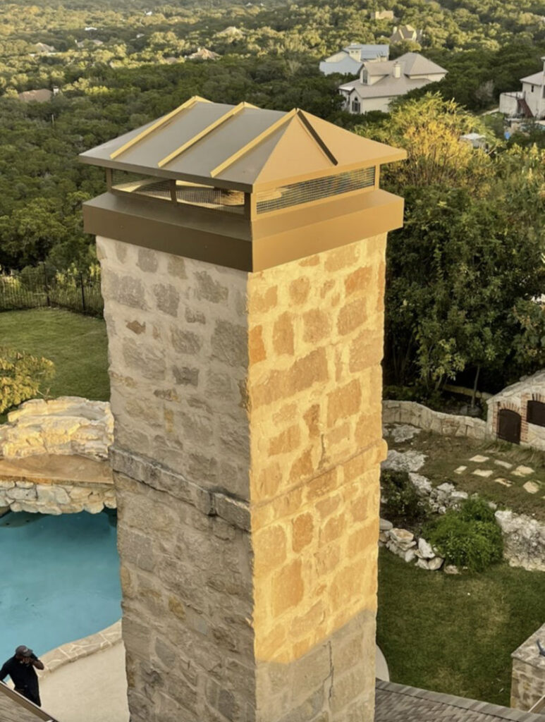 A tall stone chimney with a new cap installed by The Texan Chimney Sweep San Antonio, TX, overlooking a pool.