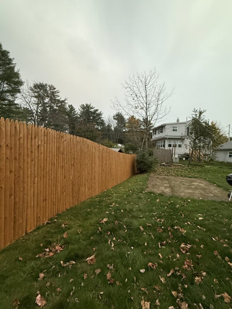 A tall wooden picket fence providing privacy for a residential backyard, installed by Triple P Fence in Augusta, ME.