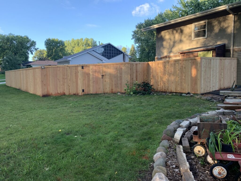 A tall wooden privacy fence with a gate providing security for a backyard by Top Notch Fence in East Bethel, MN