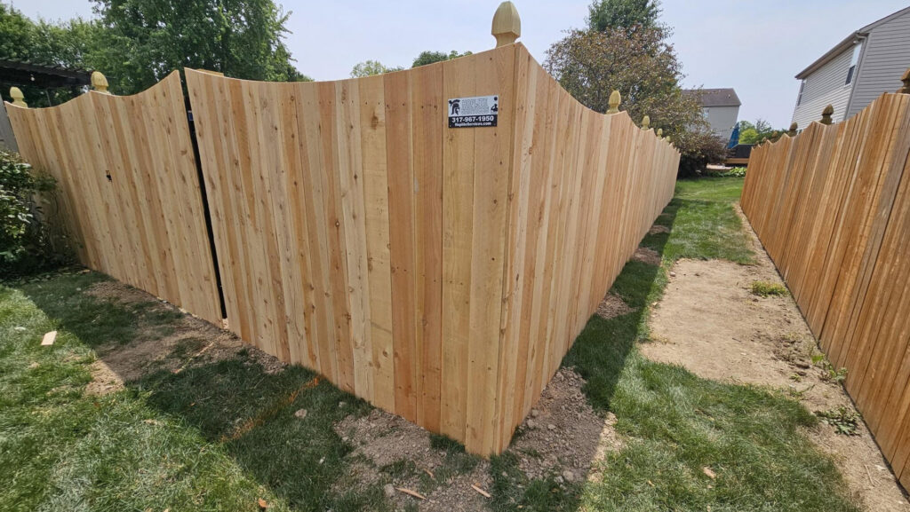 A tall wooden privacy fence with decorative post caps and a gate installed by Hoplite Services in Indianapolis, IN.