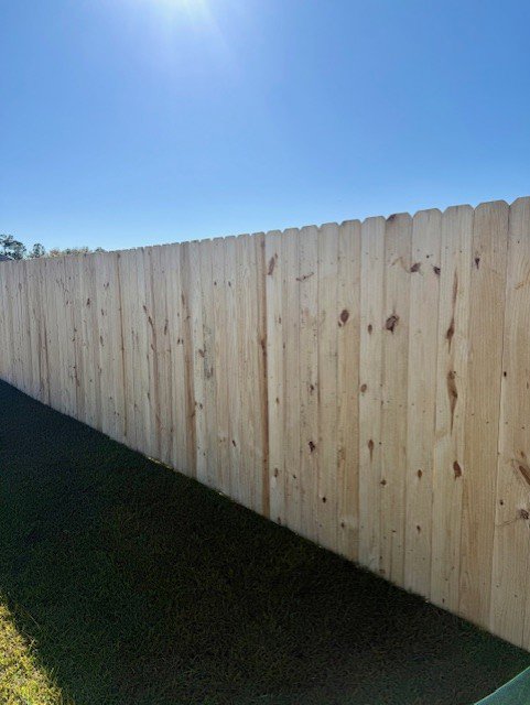 A newly installed tall wooden privacy fence under a clear blue sky by JBunlimitedfencingllc in Savannah, GA.