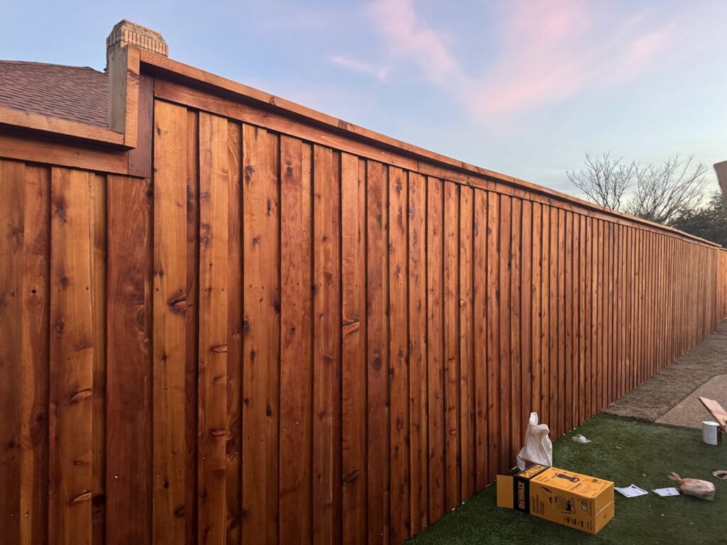 A tall, newly installed wooden privacy fence next to a residential property, built by QD & E Fencing in Fort Worth, TX.