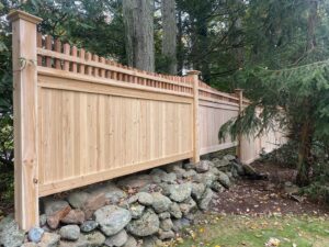 A tall wooden privacy fence with a decorative top, built on a stone wall by Flanagan Fencing in Brookfield, CT.