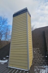 A tall, yellow-sided chimney structure on a residential roof by Professional Fireplaces and Chimney Sweeps in Huntsville, AL.