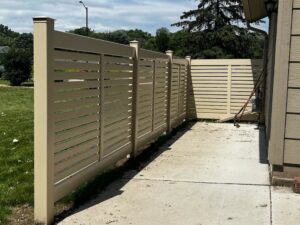 A modern tan horizontal slat privacy fence installed next to a residential building by MN Mike's Fence and Repair in Lakeville, MN.