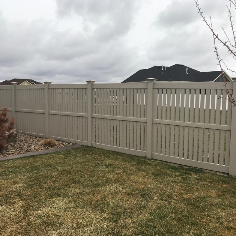 A tan semi-private fence installed in a residential backyard with green grass by Performance Fencing in Rigby, ID.