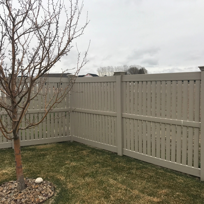 A corner section of a tan semi-private fence in a backyard with a small tree, installed by Performance Fencing in Rigby, ID.