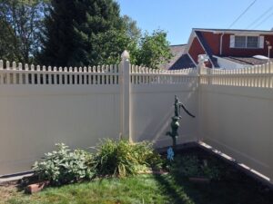 A tan vinyl privacy fence with a decorative top installed around a small garden by Schumacher Fencing, LLC in Columbus, NE.