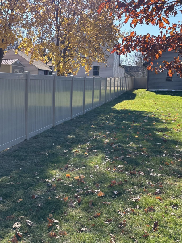 A long tan vinyl privacy fence installed in a residential backyard with autumn leaves by H&M Fencing LLC in Decatur, IN.