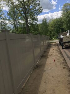 A tan vinyl privacy fence being installed along a dirt path by The Fence Dr. in Scranton, PA.