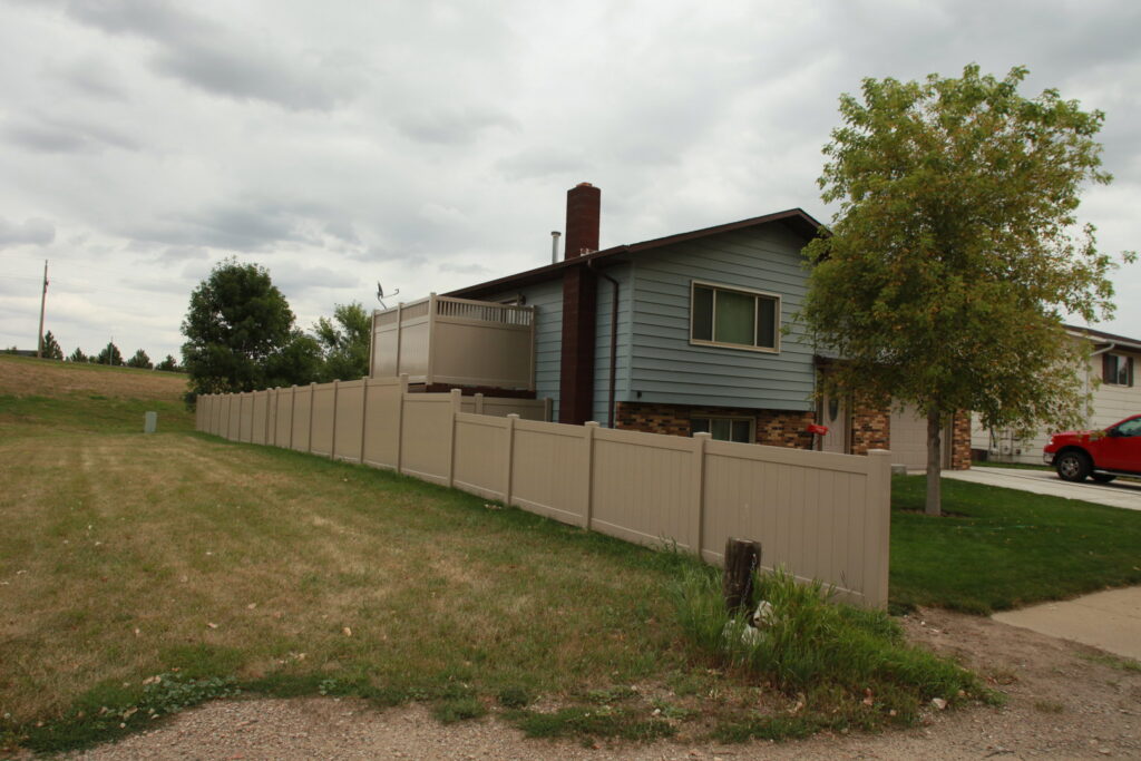 A long tan vinyl privacy fence installed along a residential property by Western Fence in Hebron, ND.