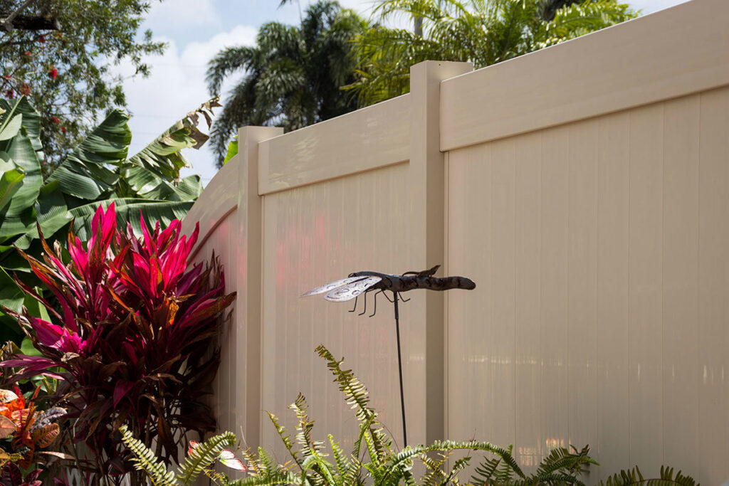A tan vinyl privacy fence installed in a lush tropical garden setting by Western Fence & Landscape Supply in Caldwell, ID.
