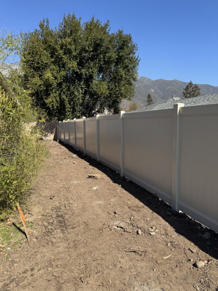 A newly installed tan vinyl privacy fence running along a dirt path in a residential area by True American Fence Supply and Construction in Anaheim, CA.