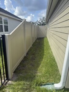 A tan vinyl fence with a matching gate installed along the side of a house by Masters Fence Contracting in Jacksonville, FL.