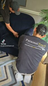 Two team members from Personal Touch Carpet Cleaning in Chicago, IL, working together to clean a dark blue sofa's upholstery.