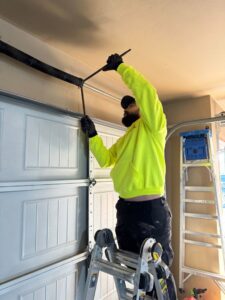 A technician from 405 Garage Pros on a ladder adjusting a garage door spring in Edmond, OK.