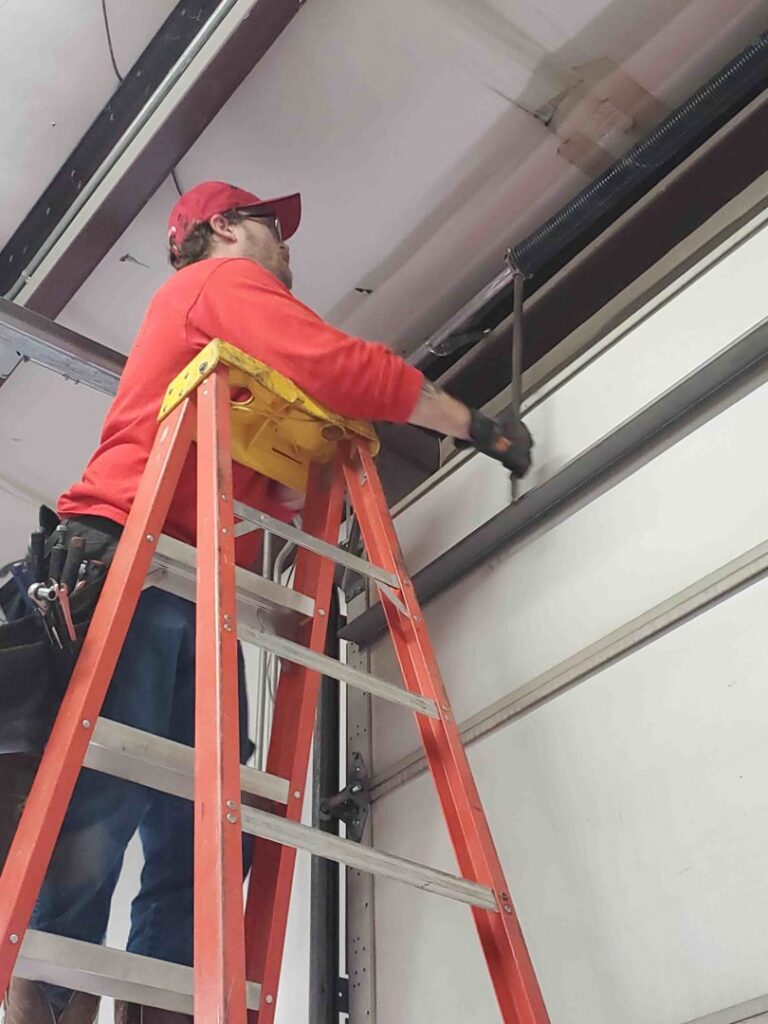 A technician adjusting garage door springs and tracks for Garage Door Specialists Of Oklahoma Inc. in Oklahoma City, OK
