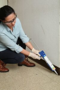 A Detourgel technician applying pest control gel with a caulk gun along a wall in Whittier, CA.