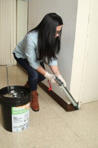 A Detourgel technician applying pest control gel with a large caulk gun along a wall in Whittier, CA.