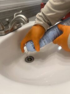 A pest control technician from Sandstorm Pest Control applying treatment to a sink drain in Chandler, AZ.