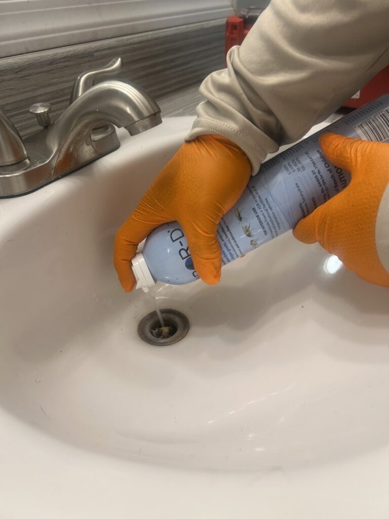 A pest control technician from Sandstorm Pest Control applying treatment to a sink drain in Chandler, AZ.