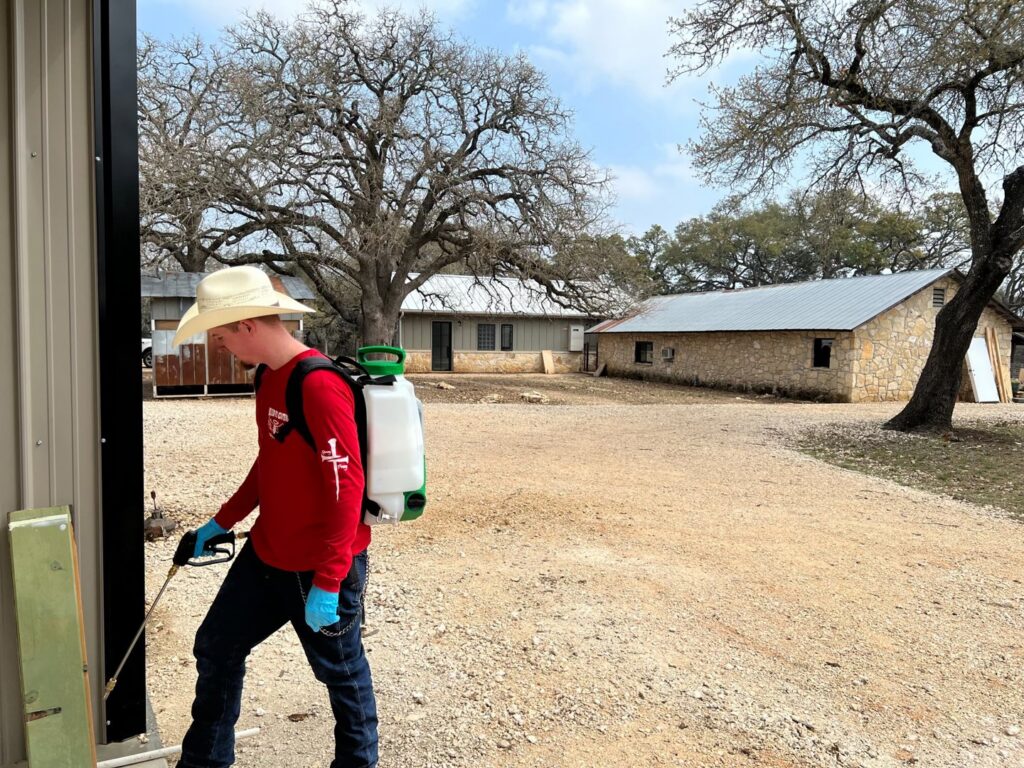 A Blessed Pest Control technician applying an exterior pest treatment to a building in San Antonio, TX