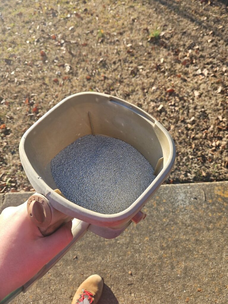 A technician from A Plus Pest Control applying granular bait or pesticide with a spreader in Huntsville, AL.