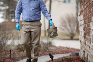 A Miller Pest & Termite technician applying granular pest control treatment around a house in Kansas City, MO