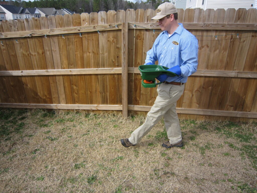 A Stomp Pest Control technician applying granular pest treatment to a residential lawn in Raleigh, NC.