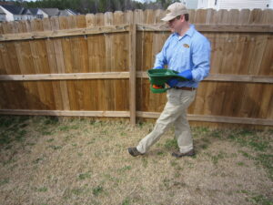 A Stomp Pest Control technician applying granular pest treatment to a residential lawn in Raleigh, NC.