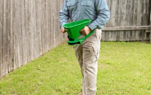 A technician applying granular pest control treatment to a lawn next to a fence for Superior Pest Management in Kannapolis, NC.