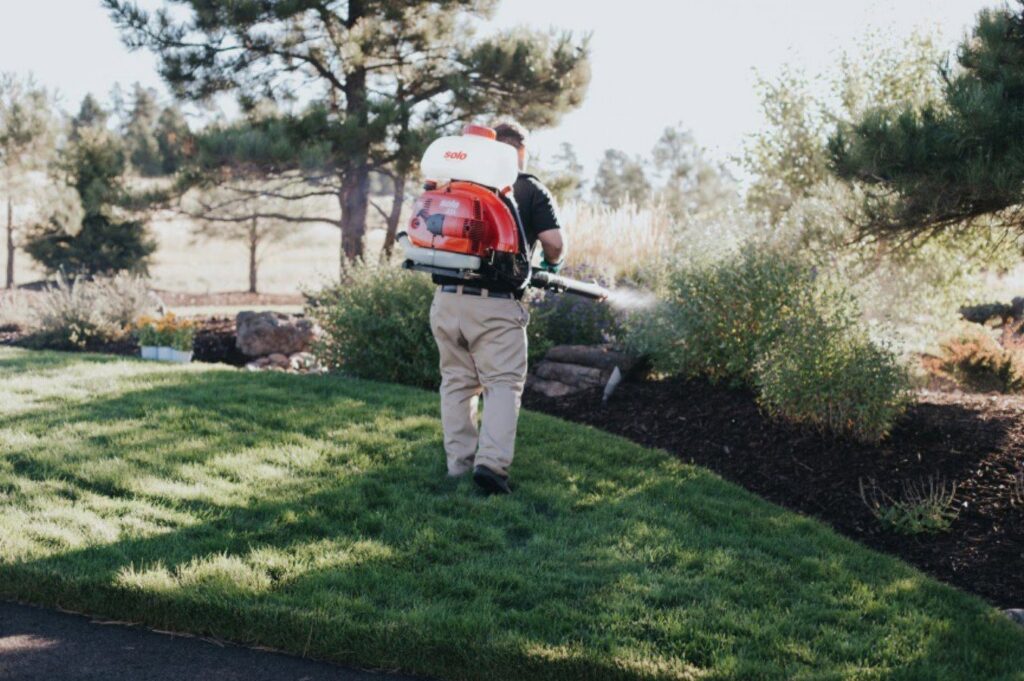 A technician from Nebraska Pro Turf & Pro Pest Solutions applying treatment to a residential lawn and shrubs in Omaha, NE.