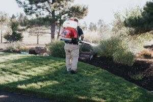 A technician from Nebraska Pro Turf & Pro Pest Solutions applying treatment to a residential lawn and shrubs in Omaha, NE.