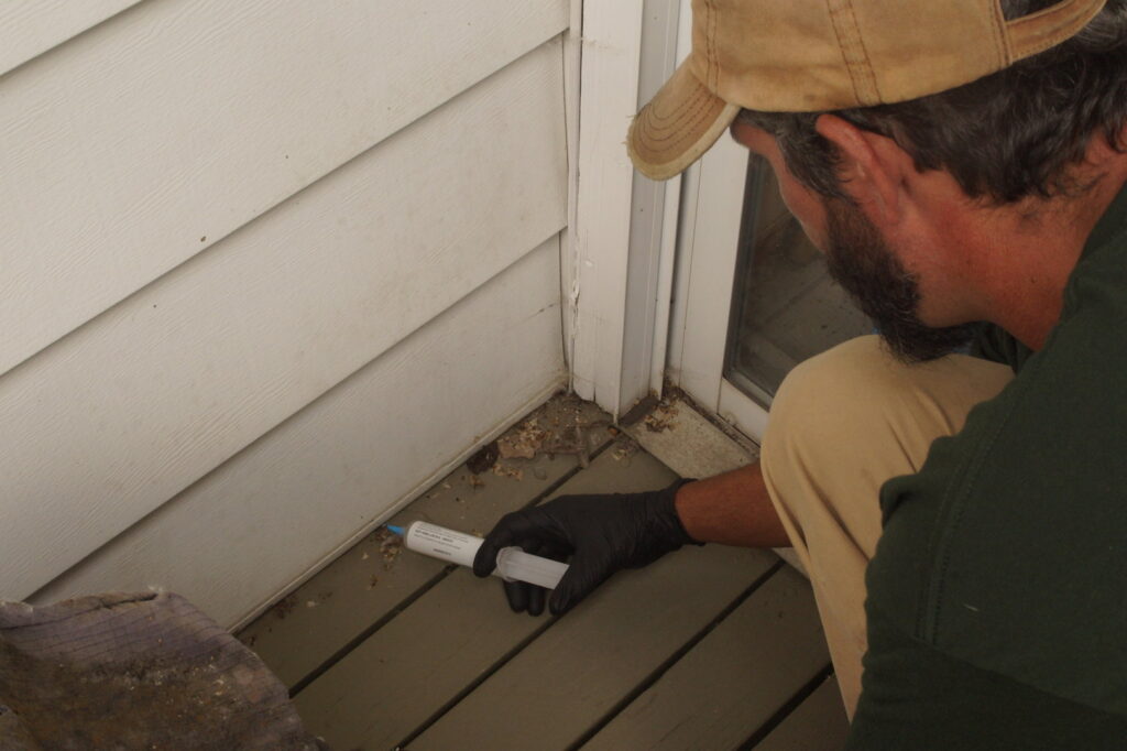 A pest control technician applying pest bait along the base of house siding for effective pest management by Midwest Pest Control in East Peoria, IL.