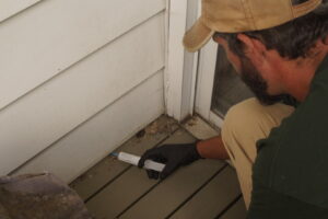 A pest control technician applying pest bait along the base of house siding for effective pest management by Midwest Pest Control in East Peoria, IL.