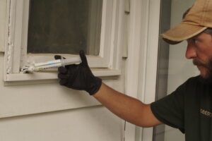 A pest control technician applying Advion Ant gel bait near a window frame as part of pest treatment by Midwest Pest Control in East Peoria, IL.