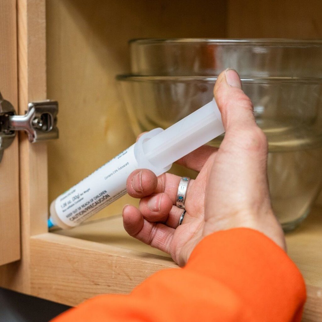 A technician applying pest control gel from a tube into a cabinet, providing targeted treatment by Rocky Mountain Pest Control in Santa Fe, NM.