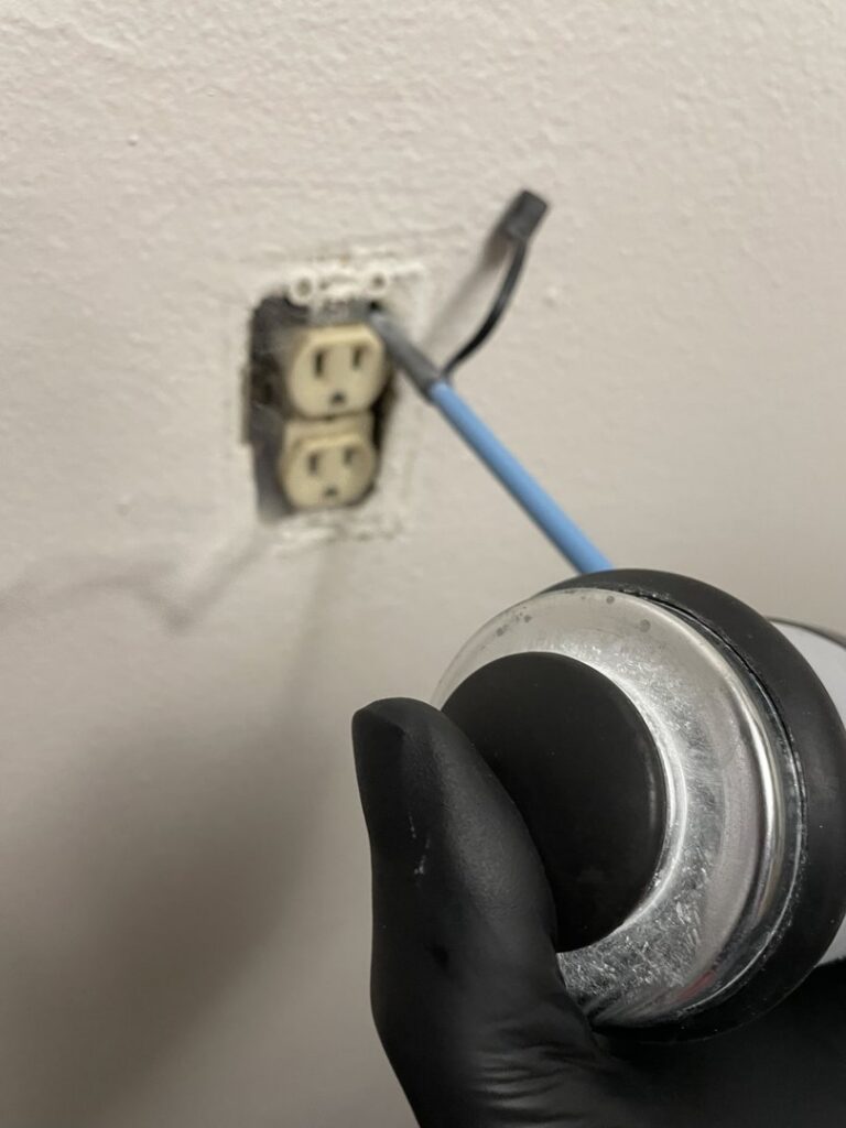 A technician applying pest treatment into an electrical outlet, a common method used by Pike Creek Exterminating in Kenosha, WI.