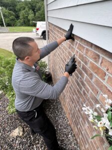 A Bye Bye Pest Solutions technician applying pest treatment to the exterior brick wall of a house in Hanover, PA.