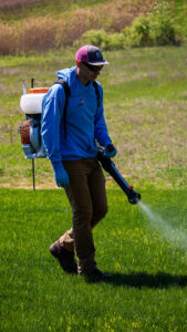 A Pest Badger technician applying a pest treatment to a lawn with a backpack sprayer in Chippewa Falls, WI.